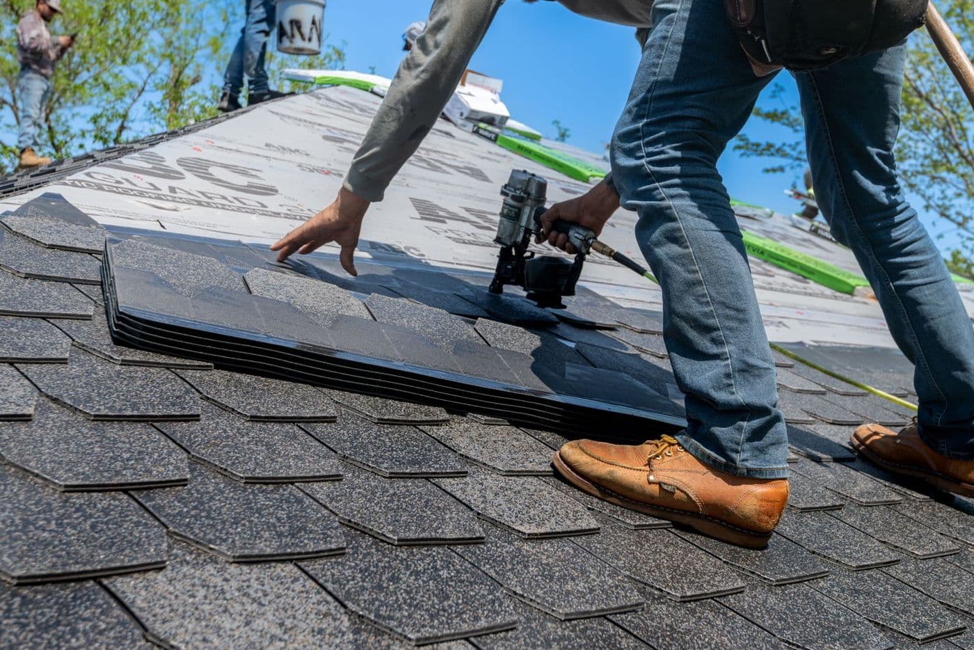 A roofer fastening architectural asphalt shingles with a nail gun